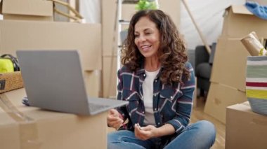 Orta yaşlı İspanyol kadın yeni evinde elinde anahtarlarla video görüşmesi yapıyor.