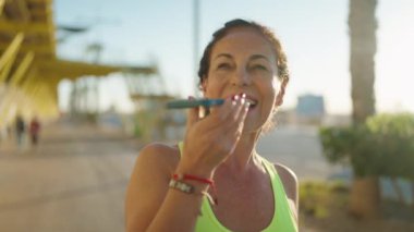 Orta yaşlı kadın spor kıyafeti giyiyor ve caddede akıllı telefondan konuşuyor.