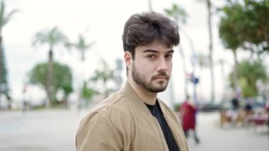 Sokağın ortasında eli kamerayla kamerayı kapatan ciddi bir ifadeyle duran İspanyol genç adam.