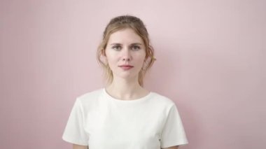Genç sarışın kadın gülümsüyor. Kendine güveniyor. Elleri pembe arka planda fotoğraf çekiyor.