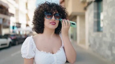 Young middle east woman smiling confident listening audio message by the smartphone at street