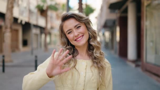 Joven Mujer Rubia Sonriendo Confiada Diciendo Hola Con Mano Calle — Vídeo de stock