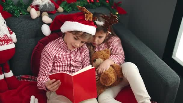 Αδελφός Και Αδελφή Ανάγνωση Βιβλίο Κάθεται Στον Καναπέ Χριστουγεννιάτικη Διακόσμηση — Αρχείο Βίντεο