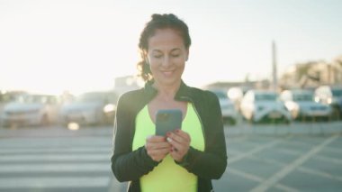 Orta yaşlı kadın spor giyer. Sokakta akıllı telefon kullanır.