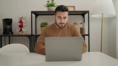 Evdeki masada dizüstü bilgisayar kullanan genç bir İspanyol.