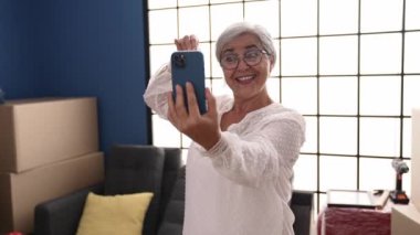 Middle age grey-haired woman choosing color to paint wall at new home