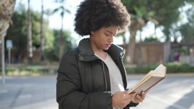 Afro-Amerikalı kadın gülerek sokakta kendine güvenen kitap okuyor.