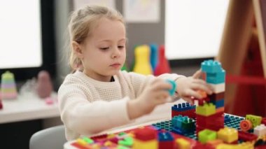Adorable blonde girl playing with construction blocks sitting on table at kindergarten