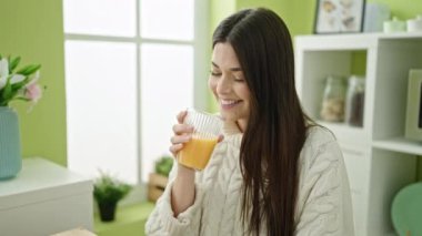 Genç ve güzel İspanyol kadın evde oturmuş portakal suyu içiyor.