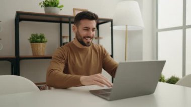 Evdeki masada dizüstü bilgisayar kullanan genç bir İspanyol.