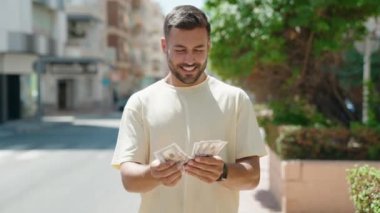 Young hispanic man smiling confident counting dollars at street