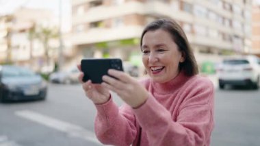 Middle age woman smiling confident watching video on smartphone at street