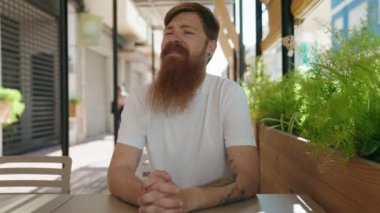 Young redhead man smiling confident sitting on table at coffee shop terrace
