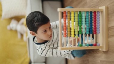 Adorable hispanic boy playing with abacus sitting on floor at home