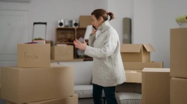 Orta yaşlı bir kadın yeni evinde akıllı telefondan konuşuyor.