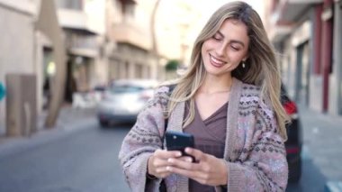 Sokakta akıllı telefon kullanan, kendine güvenen genç sarışın kadın.