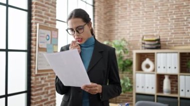 Young beautiful hispanic woman business worker reading document at office