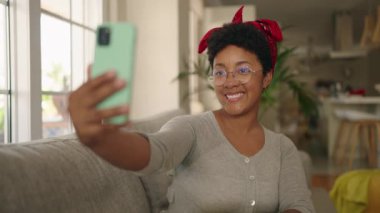 Afro-Amerikalı bir kadın evdeki koltukta video görüşmesi yapıyor.