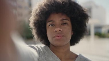 Afro-Amerikalı kadın gülümsüyor. Sokakta kamerayla özçekim yapıyor.