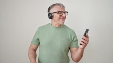 Orta yaşlı, kır saçlı, müzik dinleyen, izole beyaz arka planda dans eden bir adam.