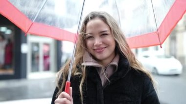 Young beautiful hispanic woman smiling confident holding umbrella at street