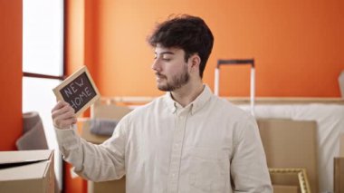 Young hispanic man smiling confident holding blackboard at new home