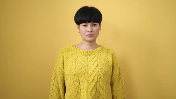 年轻的中国女人带着自信微笑 用大拇指在孤立的黄色背景上签名 — 图库视频影像