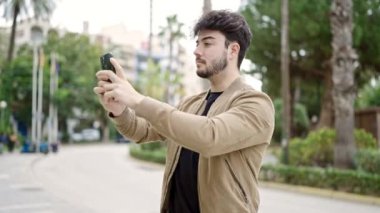 Genç İspanyol adam parkta akıllı telefondan video kaydediyor.
