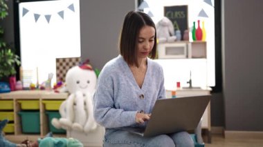 Young beautiful hispanic woman working as a teacher using laptop at kindergarten