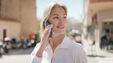 Genç sarışın kadın gülümsüyor. Kendine güveni tam. Akıllı telefondan konuşuyor.