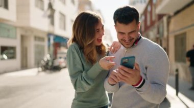Young couple smiling confident using smartphone at street