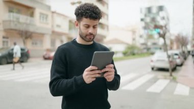 Young arab man with relaxed expression using touchpad at street