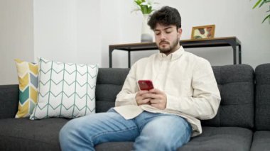 Genç İspanyol adam evde akıllı telefon kullanıyor.