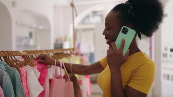 アフリカ系アメリカ人女性のお客様が衣料品店でスマートフォンで話すショッピングバッグ — ストック動画