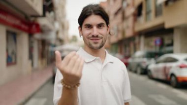 Genç İspanyol adam gülümsüyor. Kendinden emin. Sokakta el kol hareketi yapıyor.