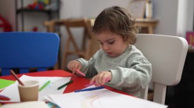 Anaokulunda masaya oturmuş kağıda resim çizen sevimli İspanyol kız öğrenci.