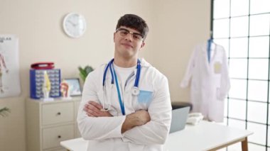 Genç İspanyol doktor gülümsüyor. Kollarını kavuşturup klinikte duruyor.