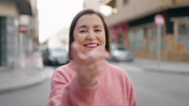 Middle age woman smiling confident doing coming gesture with finger at street