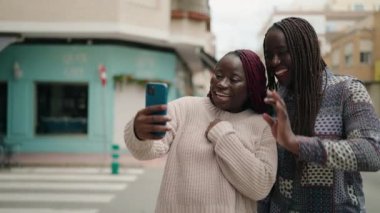 Two african american women smiling confident having video call at street