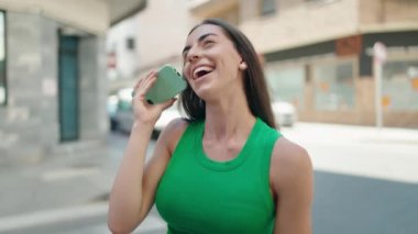 Genç, güzel, İspanyol bir kadın gülümsüyor. Caddedeki akıllı telefondan kendine güvenen bir sesli mesaj dinliyor.