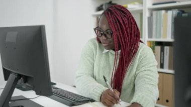 Saçları örülmüş Afrikalı bir kadın üniversite kütüphanesinde defter üzerine bilgisayar kullanıyor.