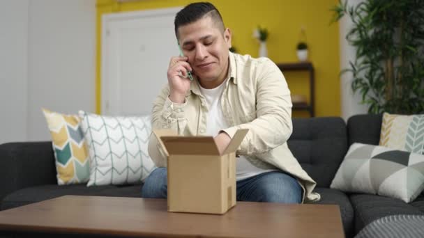 Joven Hispano Hablando Por Teléfono Desempacando Una Caja Cartón Casa — Vídeo de stock