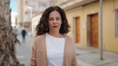 Orta yaşlı bir kadın sokakta kendine güvenerek gülümsüyor.