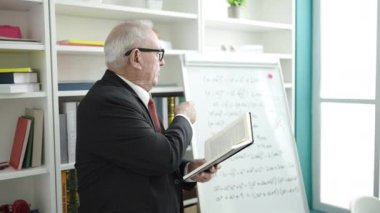 Üniversite sınıfında beyaz yönetim kurulunun yanında duran kitaplı son sınıf öğretmeni.