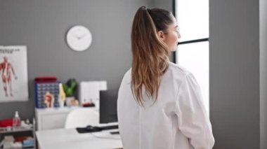 Genç, güzel İspanyol kadın doktor gülümsüyor. Kollarını kavuşturup klinikte kendine güveniyor.