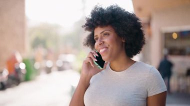 Genç Afrikalı Amerikalı kadın gülümsüyor. Kendine güveni tam. Sokakta akıllı telefondan konuşuyor.
