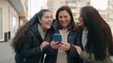 Anne ve kızları sokakta akıllı telefon kullanarak kendilerine güveniyorlar.