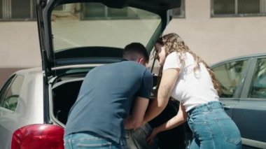 Young hispanic couple putting suitcase in car trunk at street