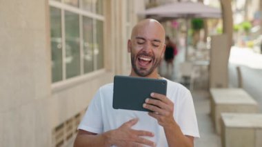 Genç kel adam gülümsüyor. Caddedeki dokunmatik evde videolar izliyor.