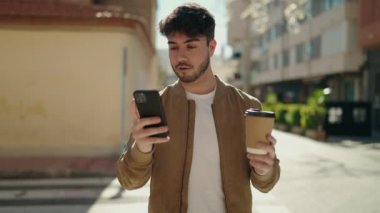 Genç İspanyol adam akıllı telefon kullanıyor, sokakta kahve içiyor.